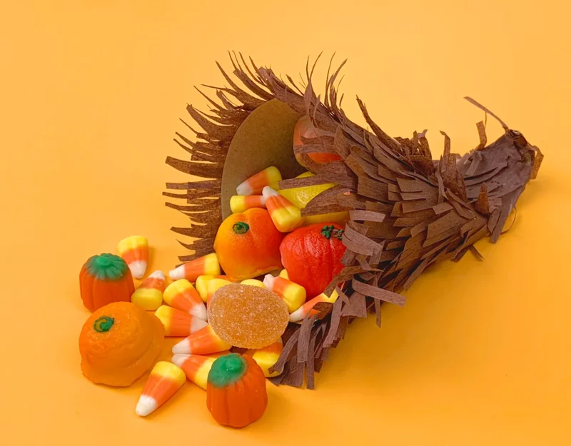 A tiny paper cornucopia made from brown fringed tissue paper with candy corn spilling out