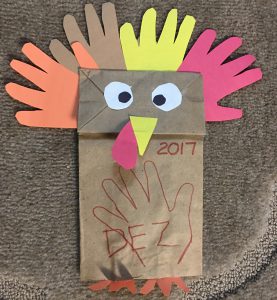 A paper bag puppet made to look like a turkey with paper cutout handprints as feathers 