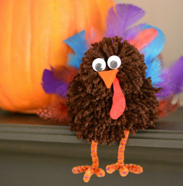 A tiny turkey is made from a brown yarn pom pom and feathers