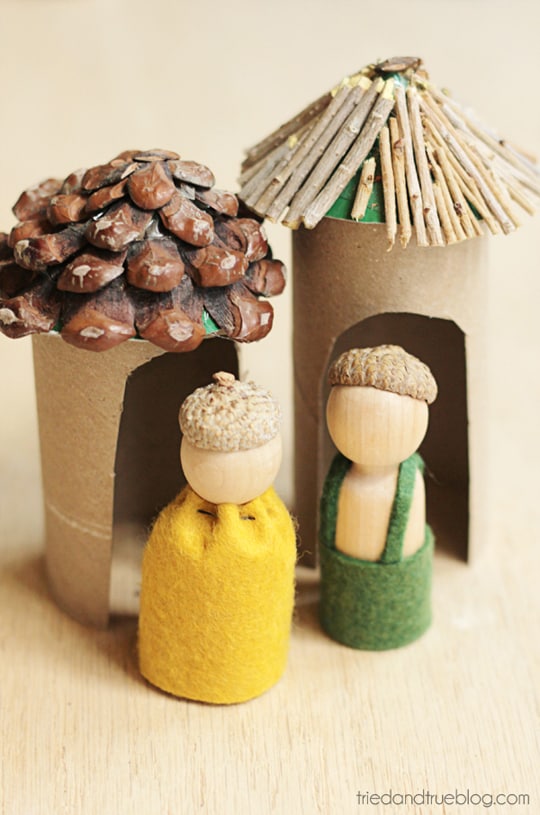 Sweet figurines made from wooden pegs standing in front of little cottages made from paper rolls