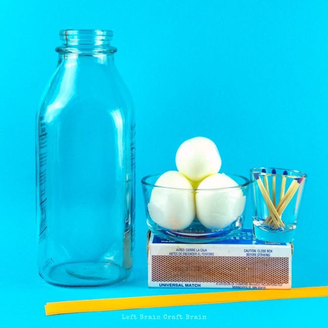 Glass bottle with bowl holding three eggs, small glass with matches sitting on a box of matches, and a yellow plastic straw, against a blue background in this example of 6th grade science fair projects.