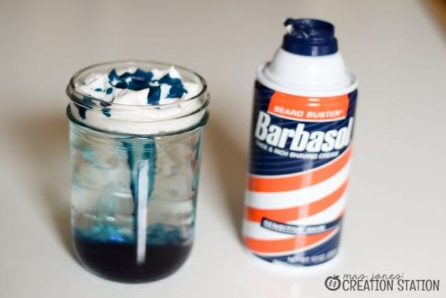 Glass jar of water with shaving cream floating on top, with blue food coloring dripping through, next to a can of shaving cream (easy science experiments)