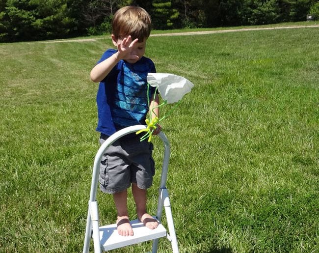 Child standing on a stepladder dropping a toy attached to a paper parachute (easy science experiments)