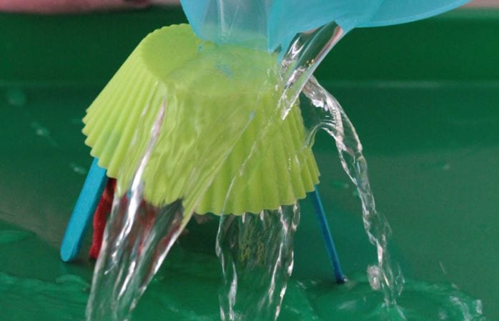 Science student pouring water over a cupcake wrapper propped on wood craft sticks (easy science experiments)