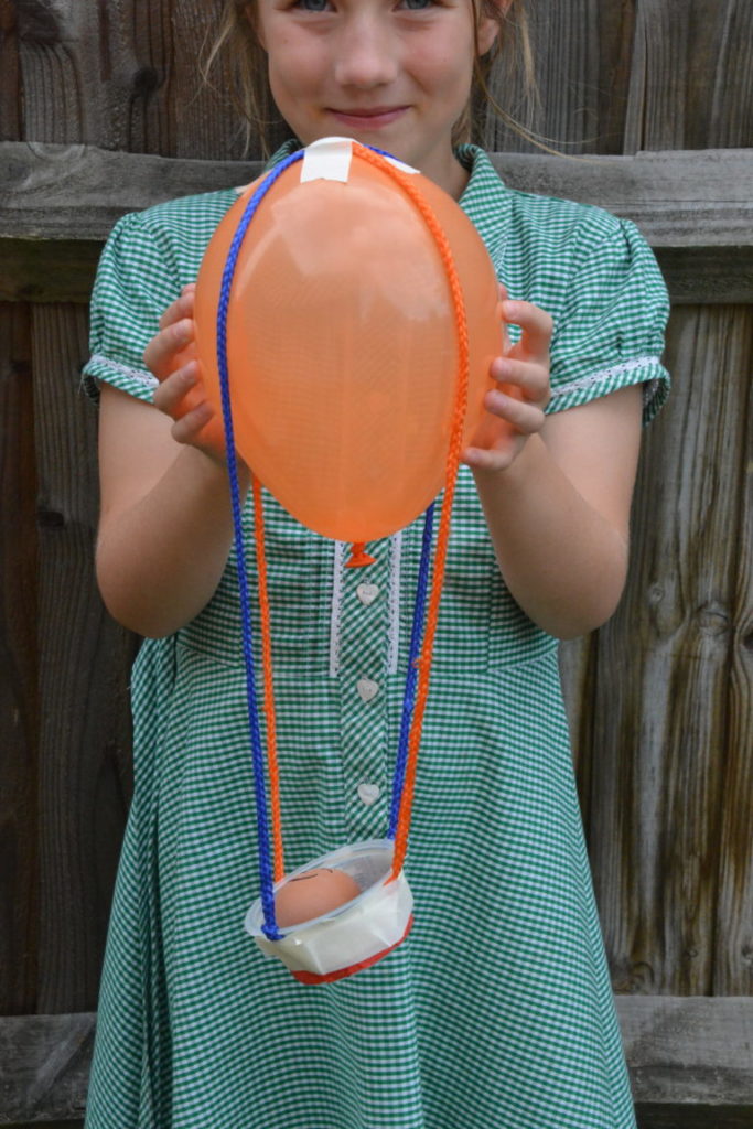 girl holding a basket attached to a balloon for an egg drop 