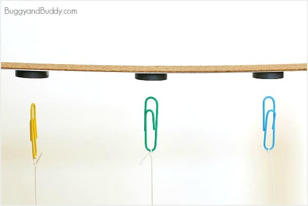 Three colored paper clips hand suspended from a wooden ruler with magnets glued to the bottom