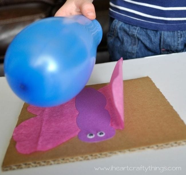 Student's hand holding a blue balloon over a tissue paper butterfly, with wing attracted to the balloon as an example of kindergarten science experiments