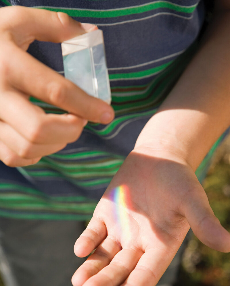 A child looks at the rainbow created on his hand as the sun shines through a prism in his other hand