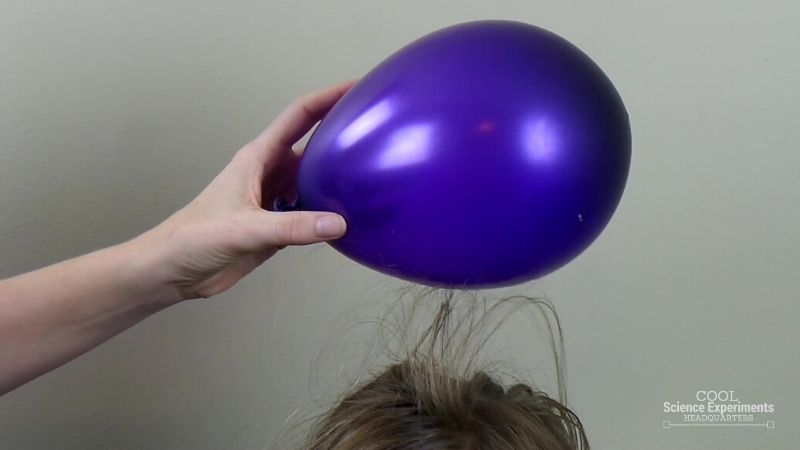 A student's hair is attracted to a purple balloon above their head as an example of kindergarten science experiments