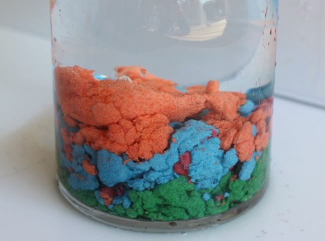 Colorful layers of hydrophobic sand in a jar of water in this example of 5th grade science