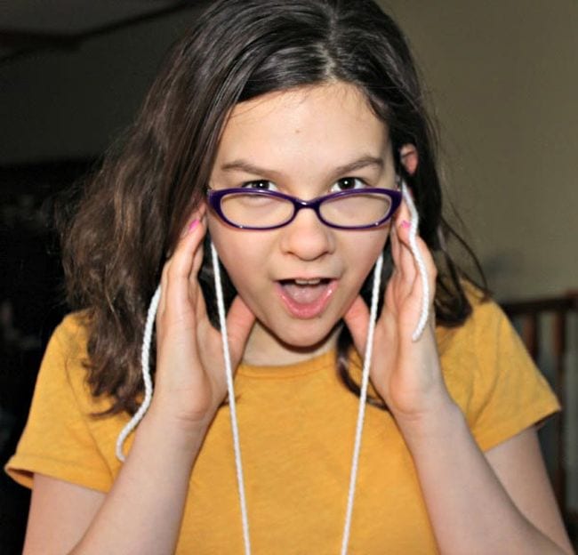 Sixth grade science student holding yarn strings to her ears and looking surprised in this example of 6th grade science fair projects