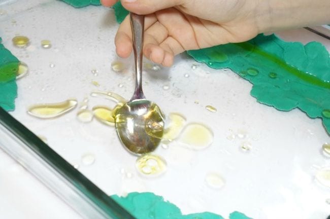 Sixth grade science student using a spoon to try to catch a puddle of oil floating on water in this example of 6th grade science fair projects