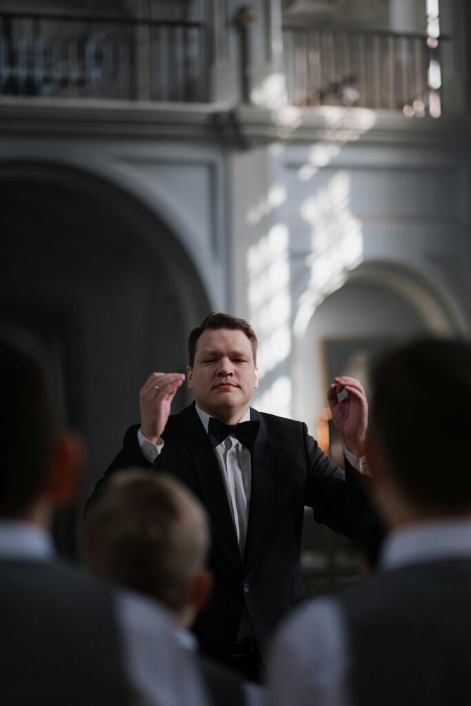 A man in a tuxedo is seen with his hands up conducting an orchestra in this example of music careers. 