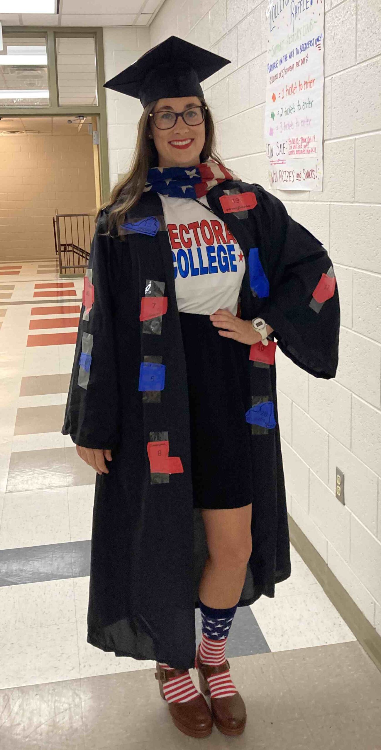 Teacher dressed in graduation cap and gown with states taped to it to represent the Electoral College