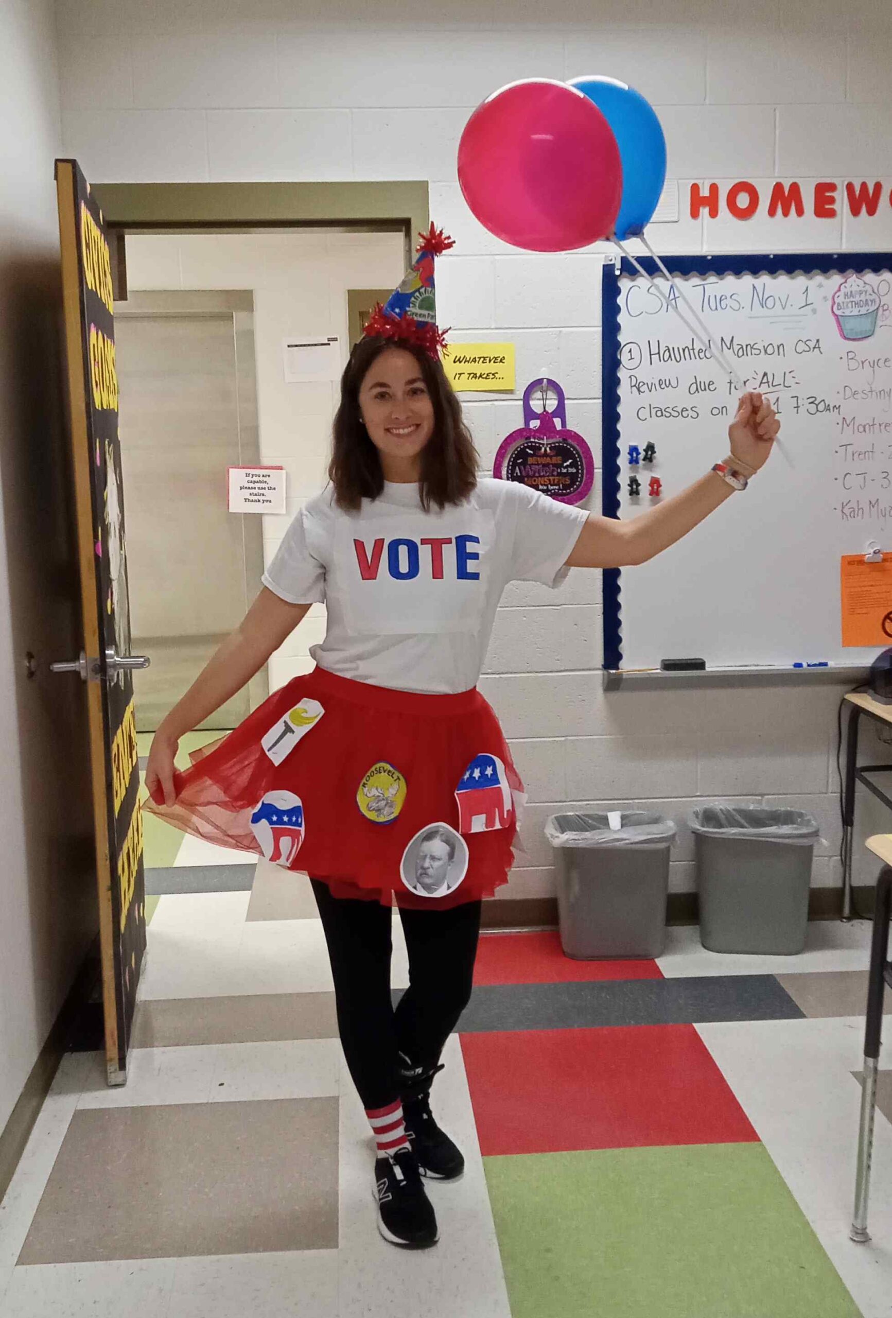 Teacher dressed in a red tutu with political symbols, wearing a party hat and carrying balloons, to represent a political party