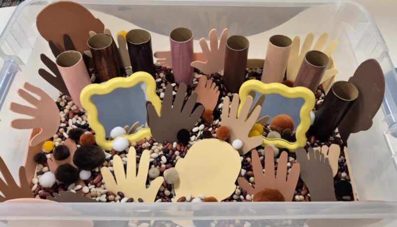 Sensory bin with foam hands and faces in a variety of skin tones, with mirrors as well