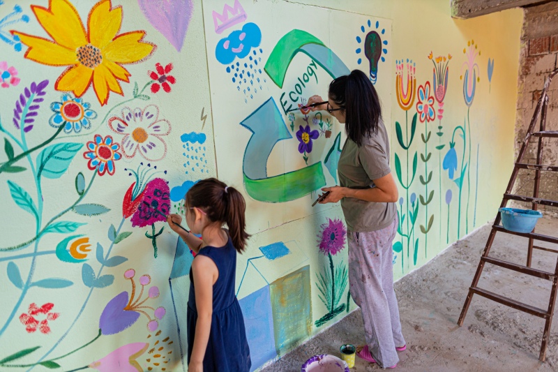 Service Learning Projects: Mural Child and teacher painting a mural in a school hallway