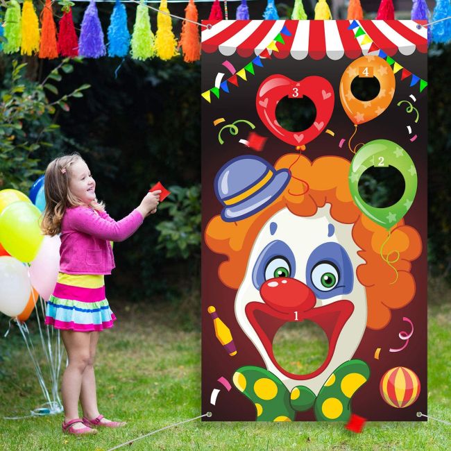Child throwing a beanbag into the open mouth of a clown printed on a vinyl banner